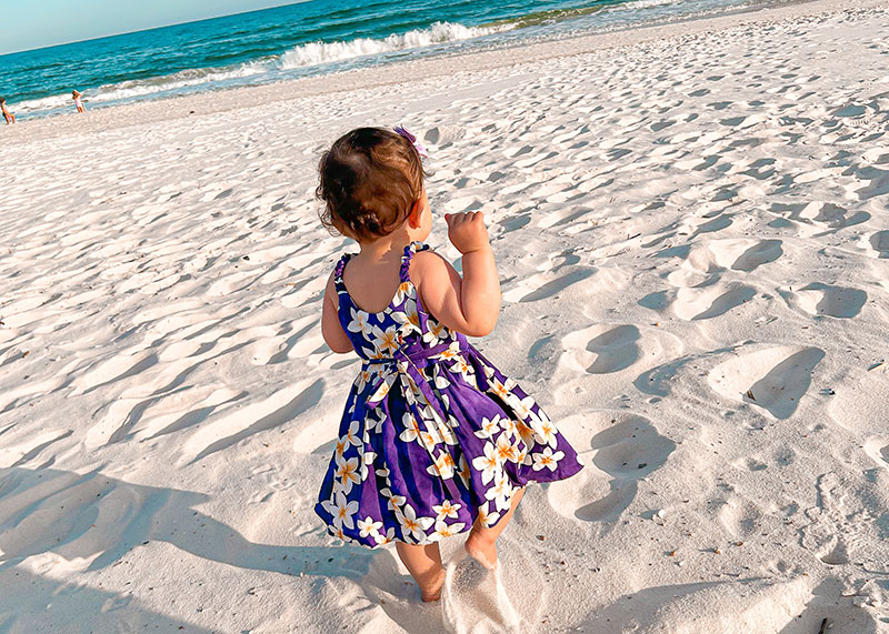 child in purple dress walking on beach